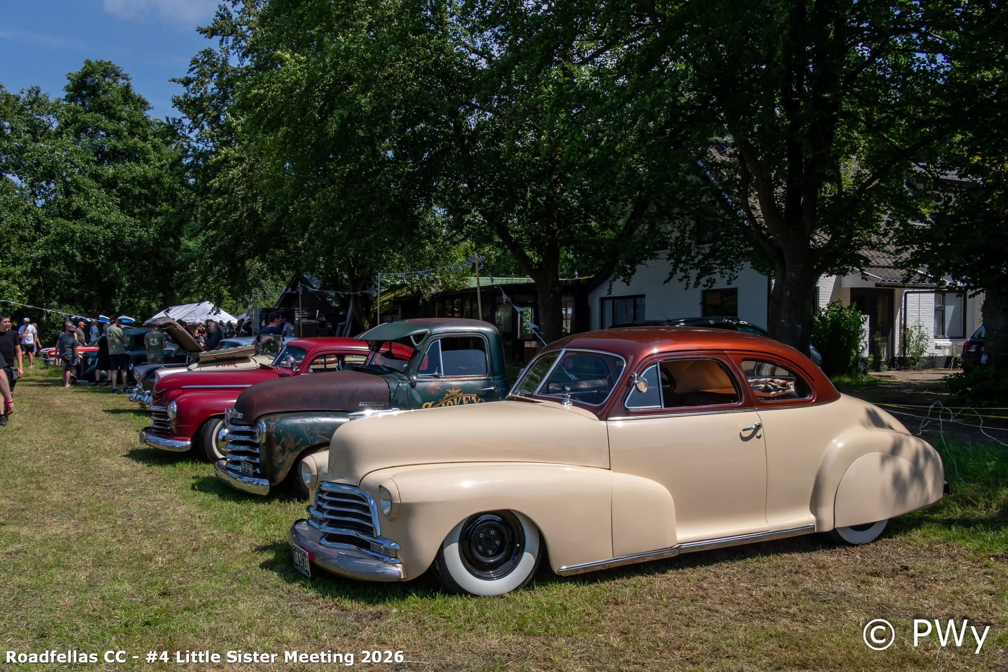 Crème custom coupé en patina-truck naast het witte gebouw van Wit Kerkje