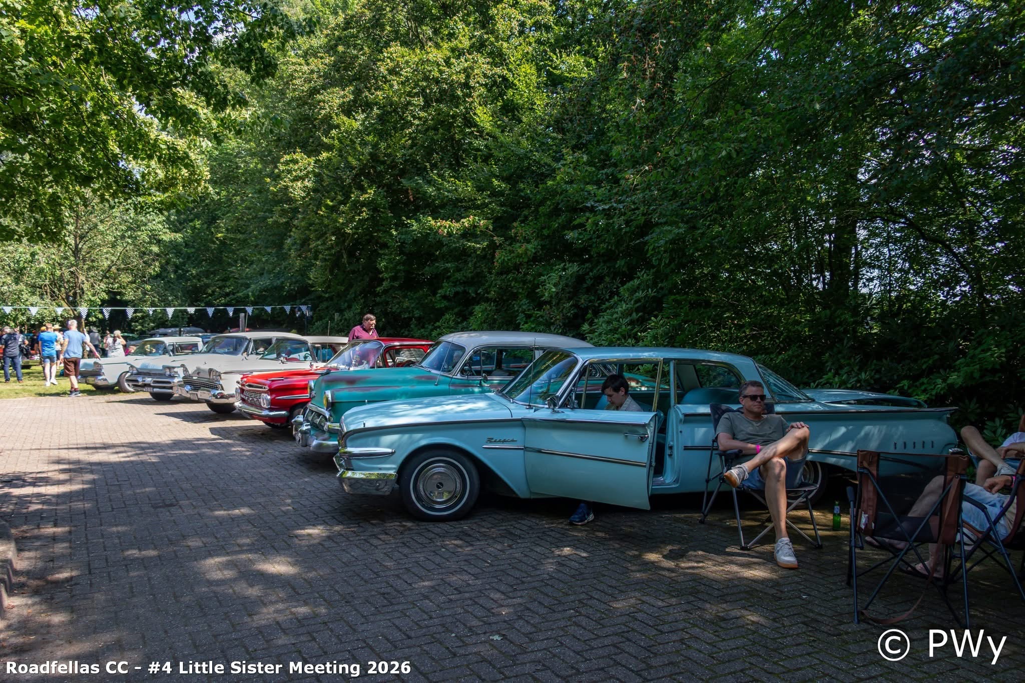 Rij klassieke auto's op de kasseiweg van Wit Kerkje met bomen op de achtergrond