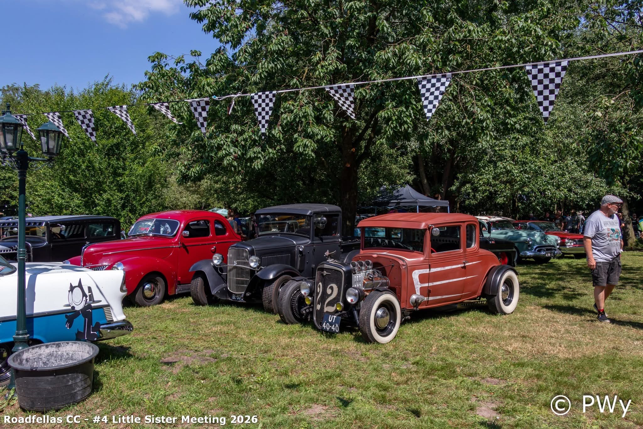 Rode coupé, zwarte Model A en terracotta Ford hot rod onder checkered bunting bij Wit Kerkje