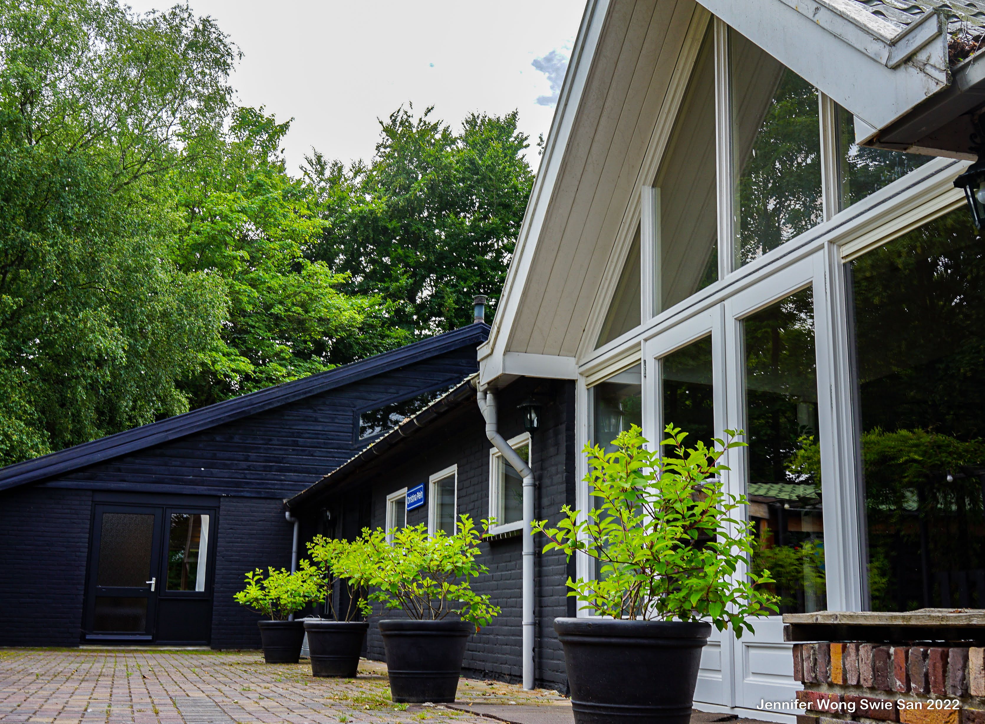 Zwart bijgebouw van Wit Kerkje met grote glazen gevel, plantenpotten en bakstenen binnenplaats