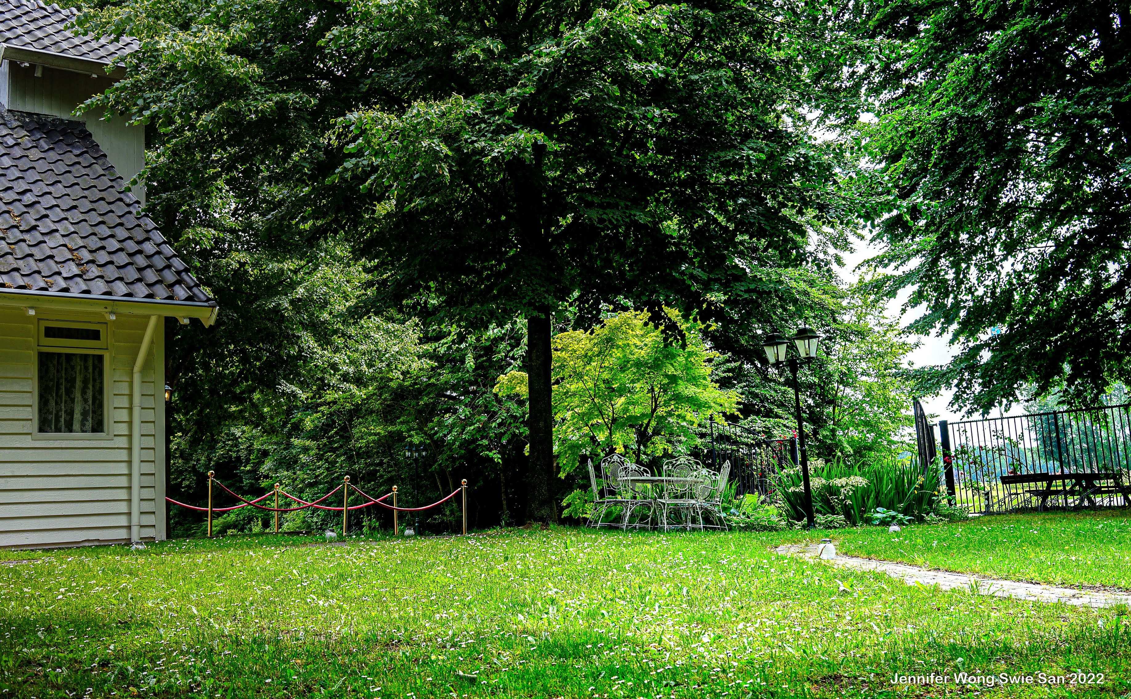 Romantische tuinhoek met wit ijzeren tafel en stoelen, lantaarnpaal en weelderig groen bij Wit Kerkje
